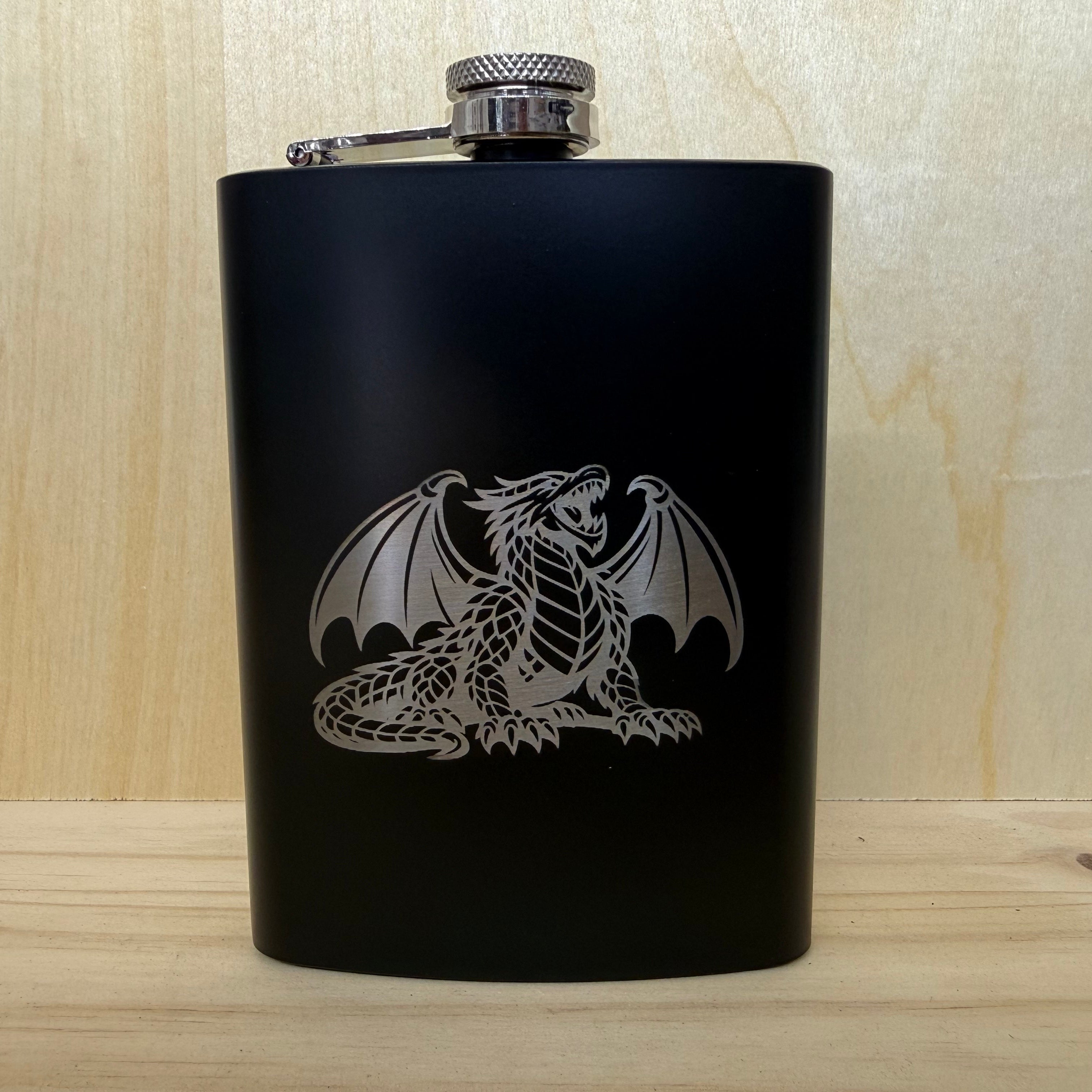 Black flask with a silver dragon design on a wooden surface
