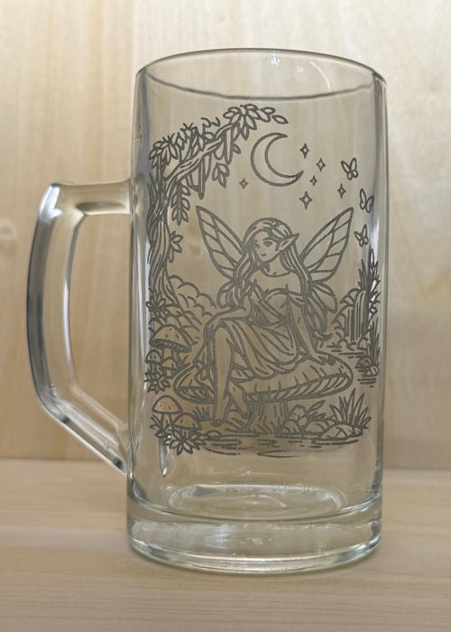 Glass mug with engraved fairy design on a wooden surface