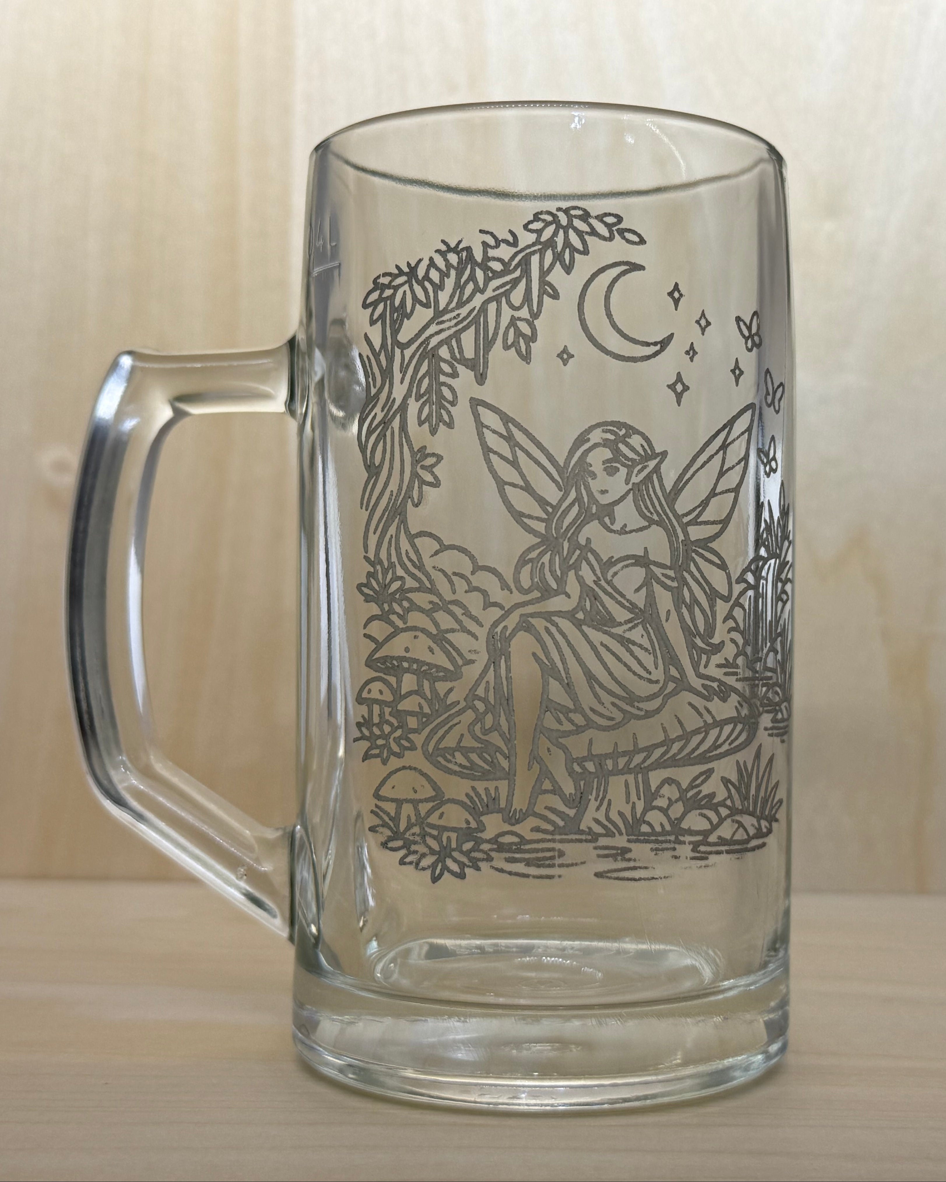 Clear glass mug with fairy design on a wooden surface