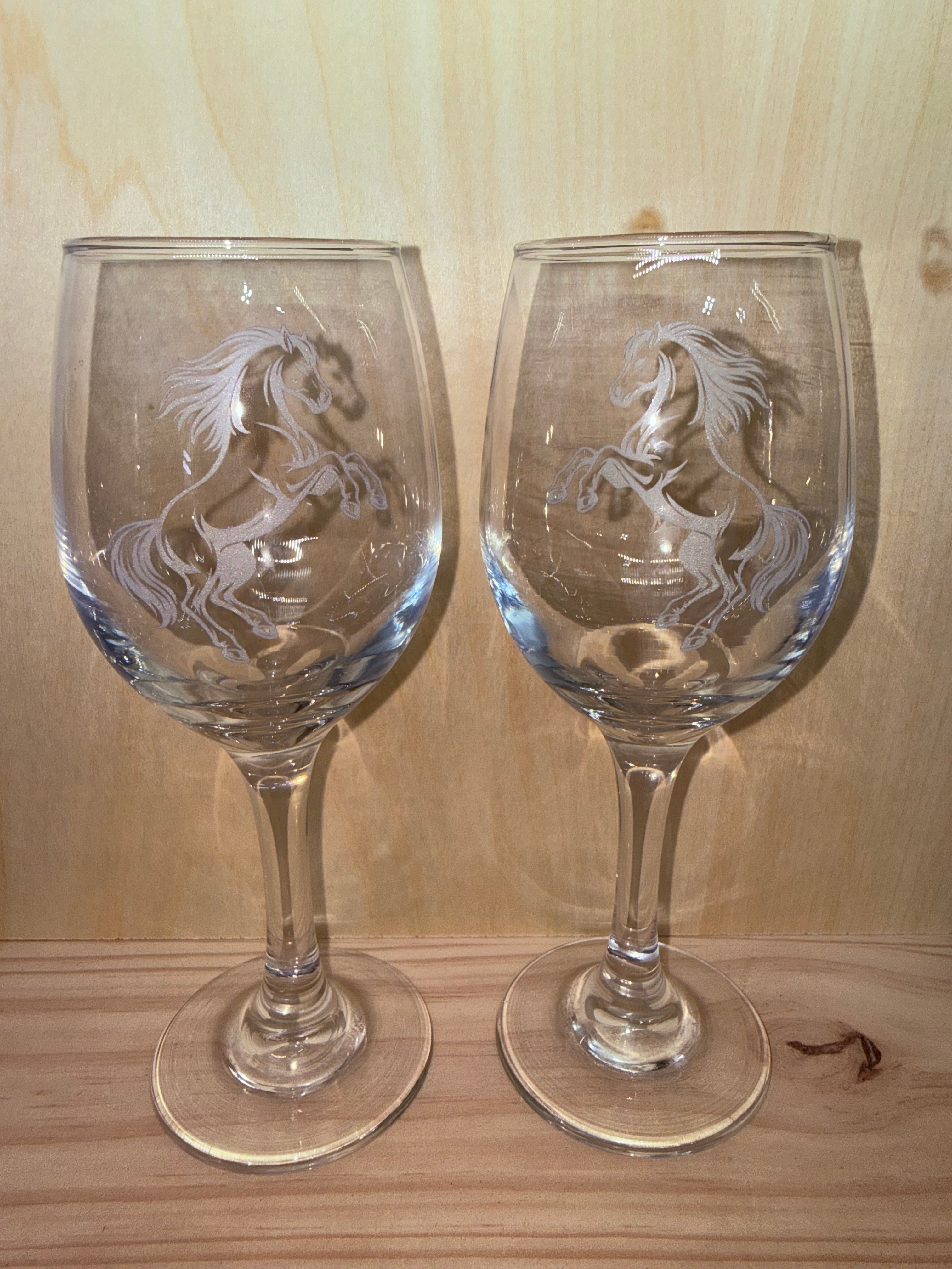 Two crystal wine glasses with engraved designs on a wooden surface