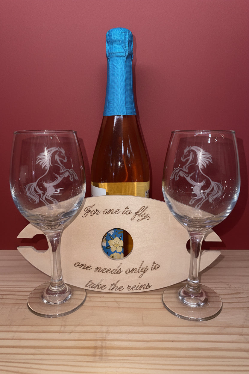 Two wine glasses with engraved designs and a bottle of champagne on a wooden surface.